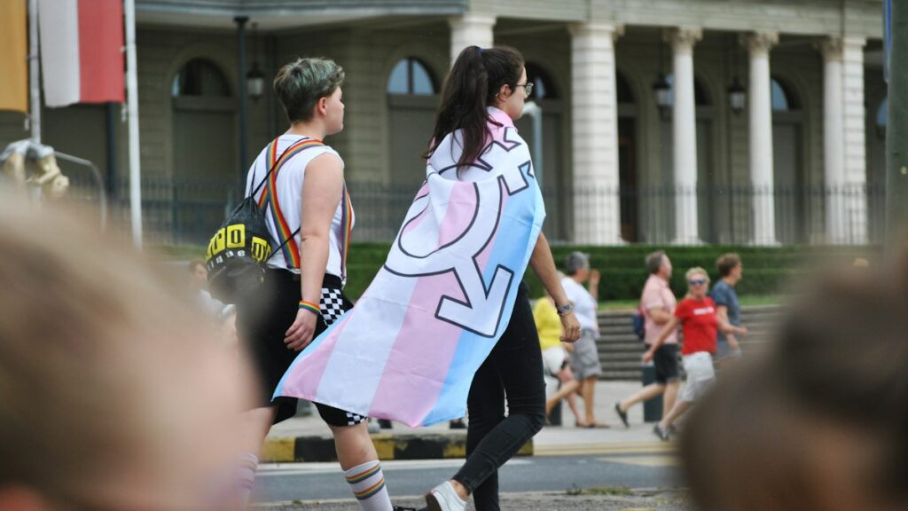 Persona de espaldas con la bandera trans sobre los hombros en una marcha